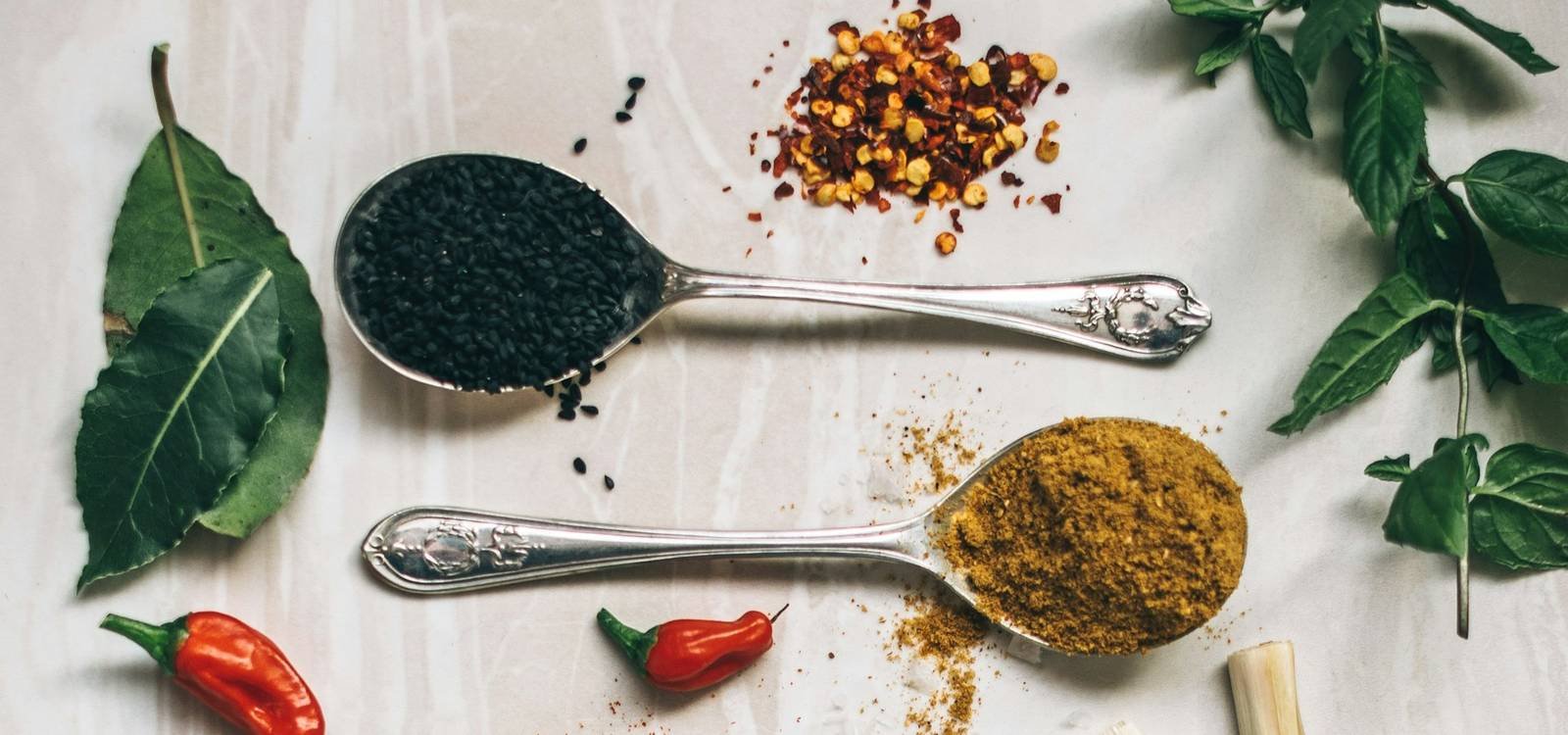 Spices, chillies and salt on spoons on a pale surface