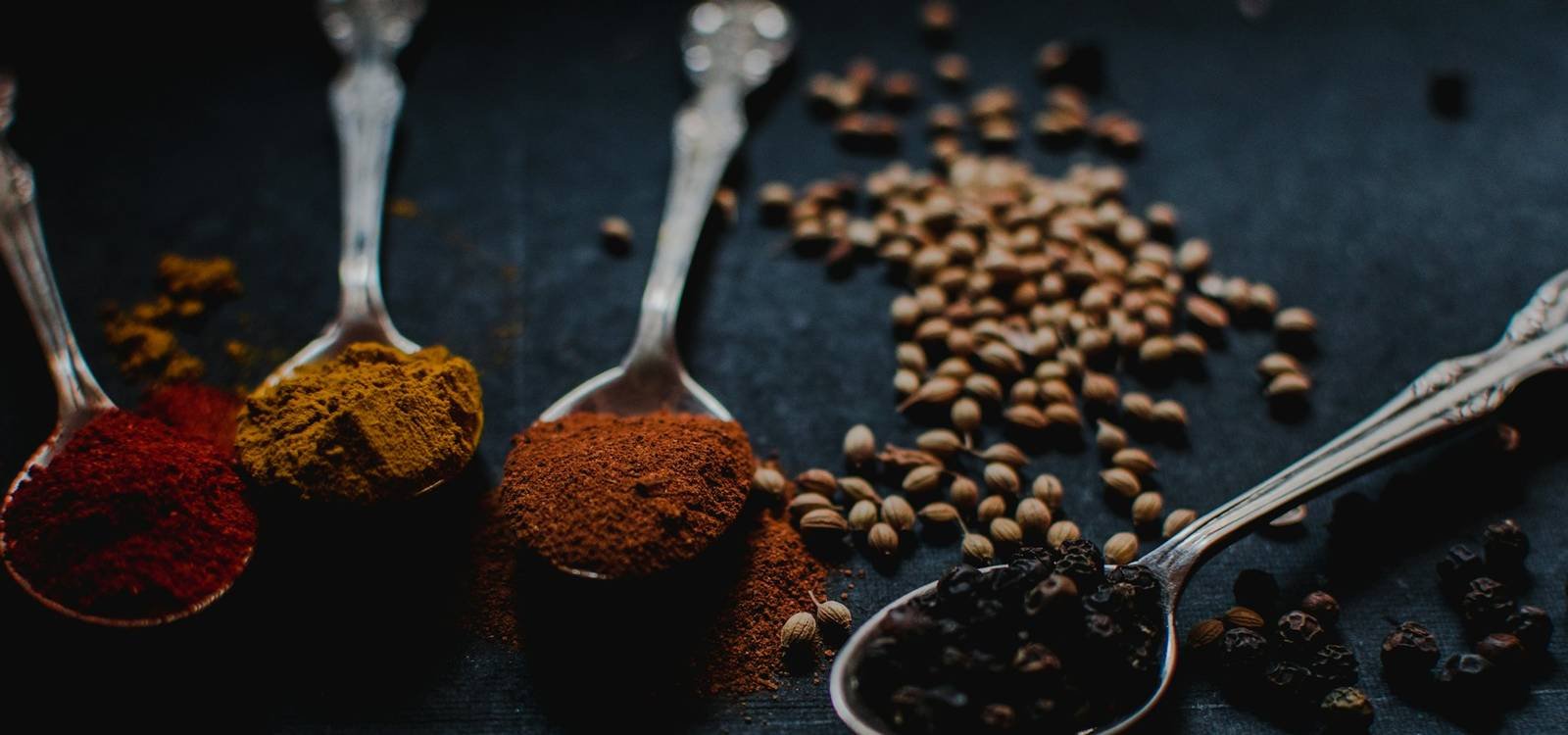 Spices on antique spoons against a dark background