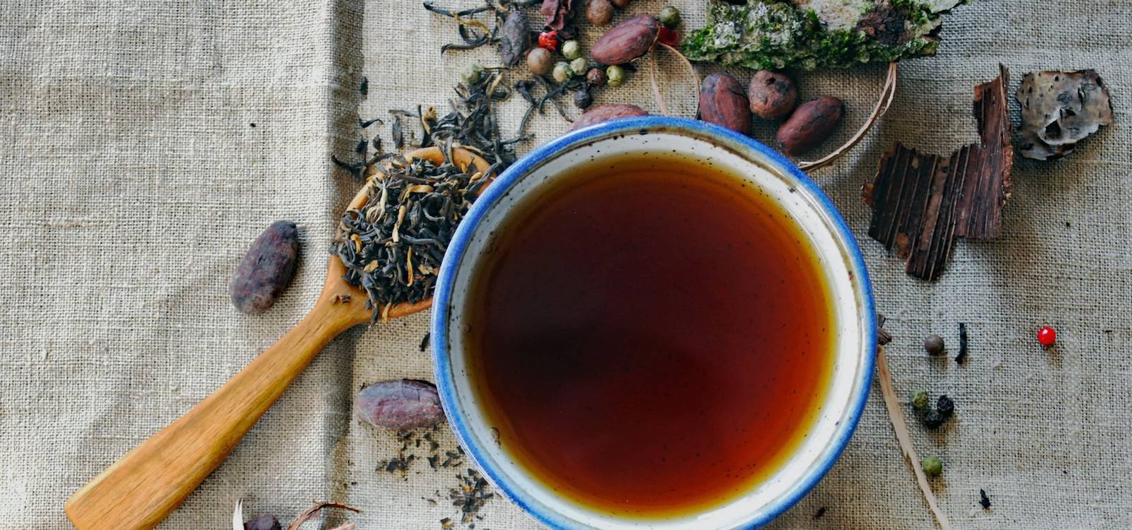 A bowl of tea surrounded by whole spices on linen