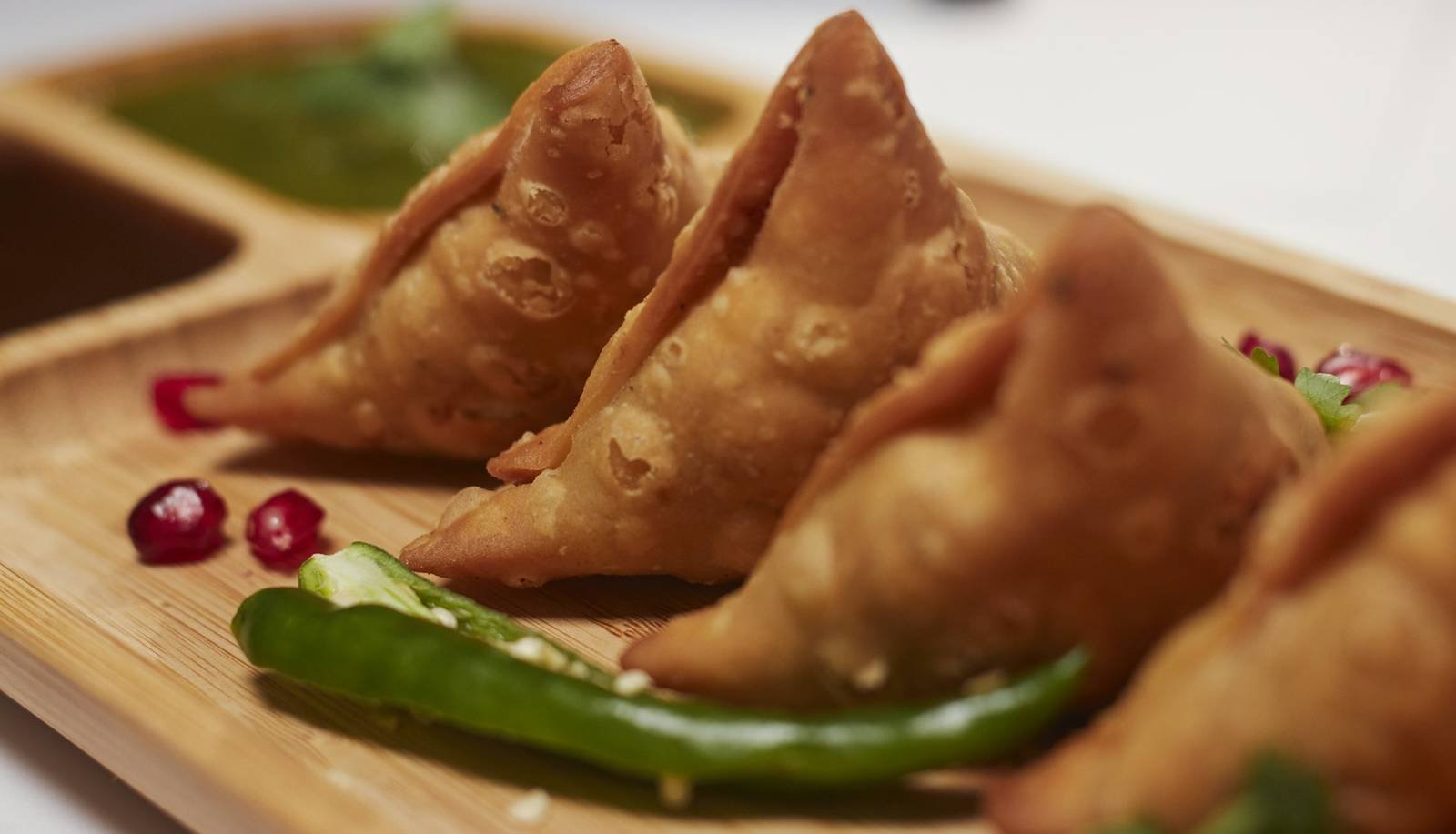 Golden samosas served with green chutney on a wooden board